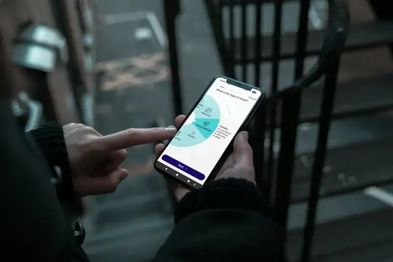 Hands holding a smartphone showing the HaZapp app's noise hazard category selection screen