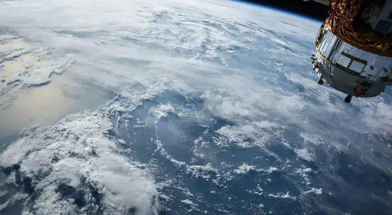 View of Earth's ocean and clouds from low-Earth orbit, with a satellite in frame